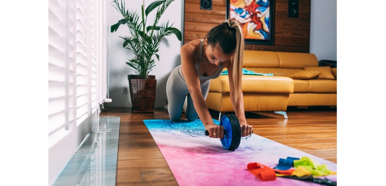 ćwicząca dziewczyna z kólkiem do brzucha i gumami na niebieskiej maćie fitness