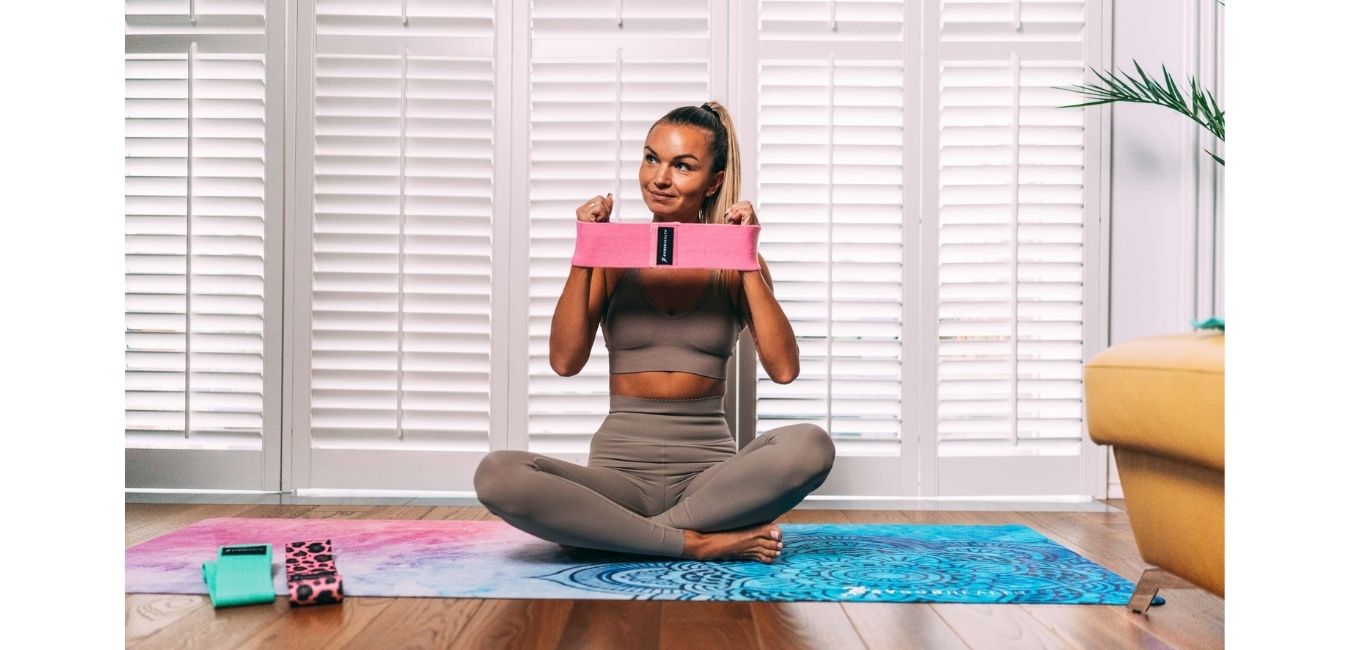 trening w domu z gumami oporowymi materiałowymi na kolorowej maćie do jogi ćwicząca dziewczyna
